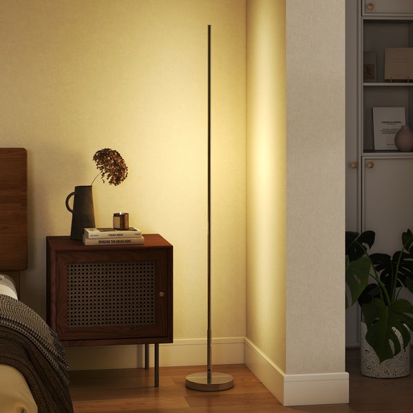 Schlanke, minimalistische LED-Stehleuchte in einer Zimmerecke neben einem Nachttisch, strahlt warmes Licht an die Wand.