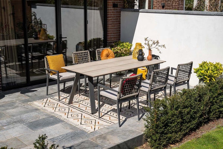 Modernes Garten-Set bestehend aus Esstisch mit Tischplatte in Holzoptik und sechs grauen Gartenstühlen auf einer Terrasse mit Außenteppich.