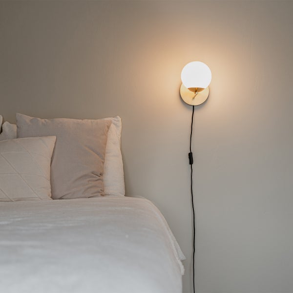 Wandleuchte mit einem kugelförmigen Lampenschirm über einem Bett.