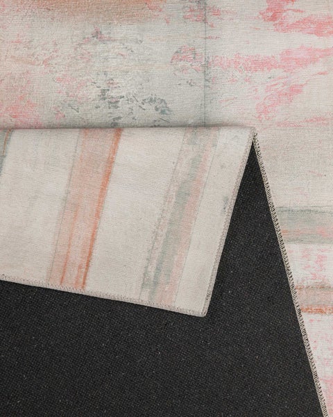 Teppich mit abstraktem Muster in Grau, Rosa und Orange, die umgeknickte Ecke zeigt die strukturierte Rückseite.