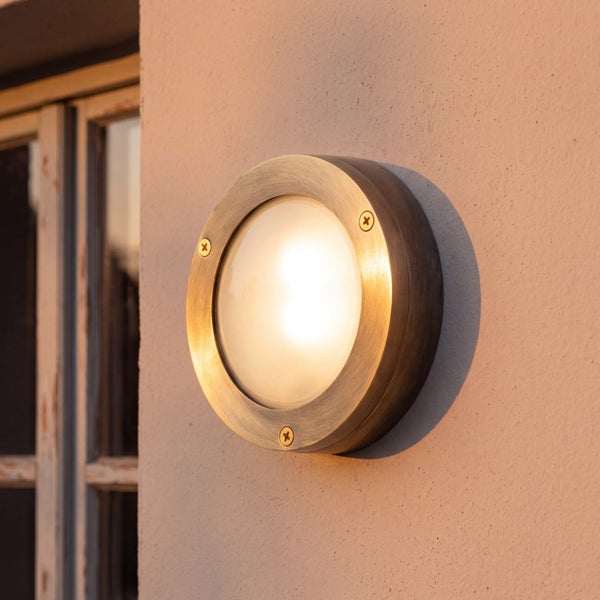 Runde Außenwandleuchte aus Metall mit mattiertem Glas und sichtbaren Schrauben, montiert an einer Wand neben einem Fenster.