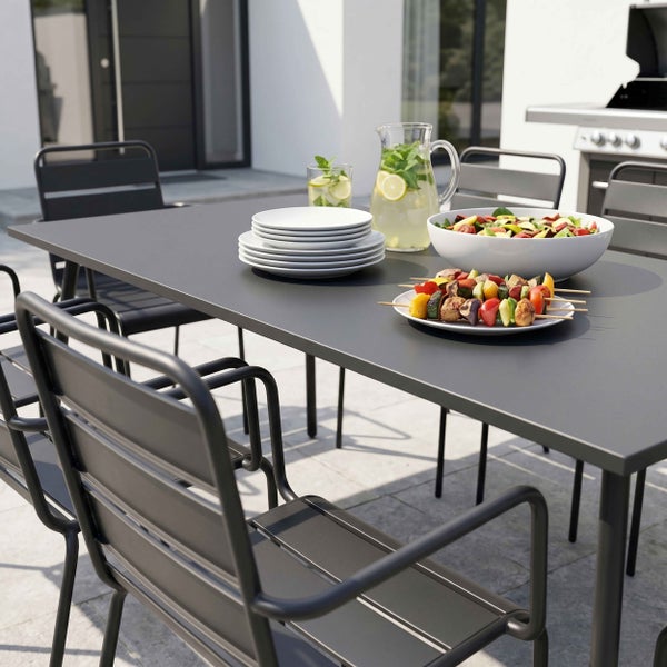 Moderne Garten-Essgruppe aus Metall mit grauem rechteckigem Tisch und passenden Stapelstühlen auf einer hellen Terrasse, gedeckt mit Speisen.