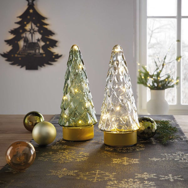 Dekorative Weihnachtsszene mit beleuchteten Glasbäumen und goldenen Ornamenten auf einem Tischläufer mit Schneeflockenmuster