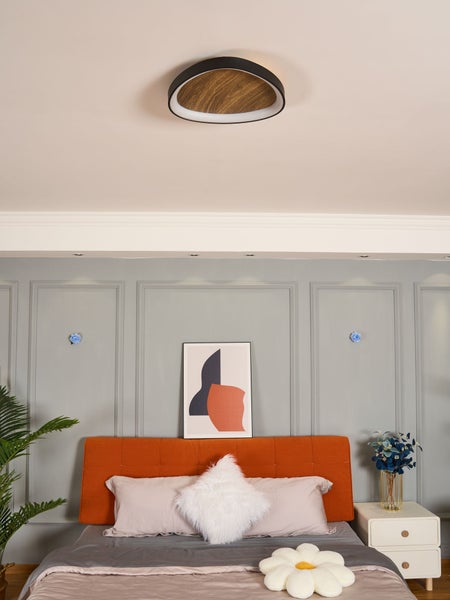 Moderne LED-Deckenleuchte mit Holzoptik-Mitte und schwarzem Rahmen in einem Schlafzimmer mit grauem Wandpaneel und orangefarbenem Bettkopfteil.