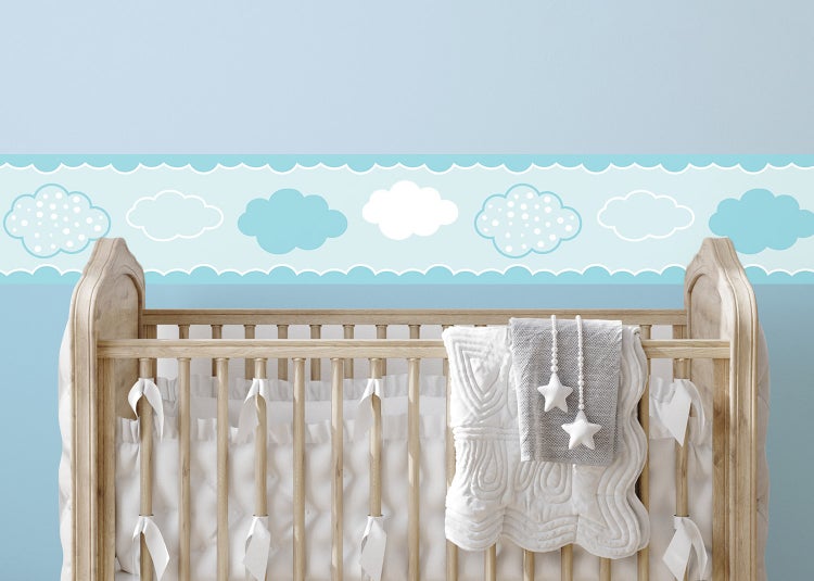 Tapetenbordüre mit Wolkenmotiv in einem hellen Kinderzimmer über einem Kinderbett aus Holz.