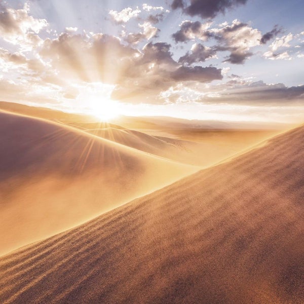 Wüstenlandschaft mit Dünen unter einem Himmel mit Wolken und Sonnenstrahlen