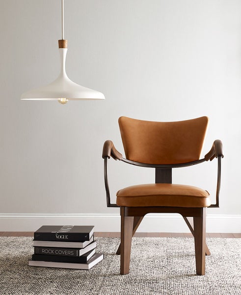 Szene mit einer weißen Pendelleuchte, einem Sessel mit Armlehnen und einem Bücherstapel auf einem gemusterten Teppich.