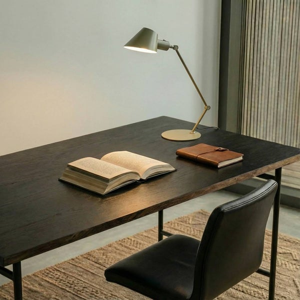 Arbeitsplatzszene mit Schreibtischlampe, offenem Buch, Notizbuch und Bürostuhl.