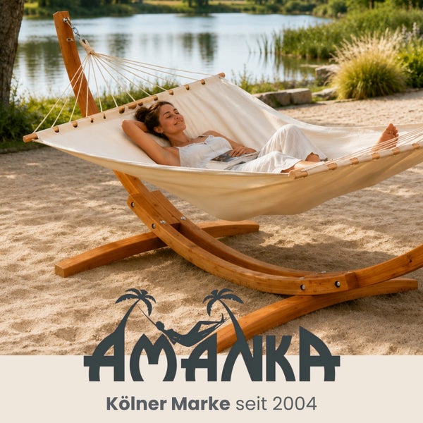 Stoffhängematte mit geschwungenem Holzgestell auf einer Sandfläche an einem See, helle und entspannte Atmosphäre. Amanka Logo.