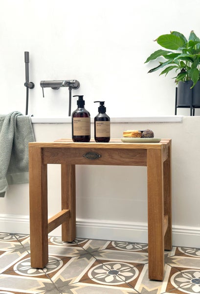 Badezimmerhocker aus Holz mit Handseife und Lotion der Marke Meraki sowie Badezusätzen auf einer Ablage