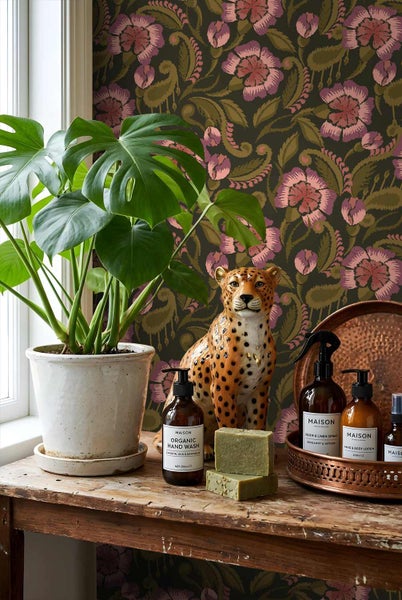 Vliestapete mit floralem Paisley-Muster hinter einer Monstera-Pflanze, einer Gepardenfigur und Pflegeprodukten auf einem rustikalen Holztisch.