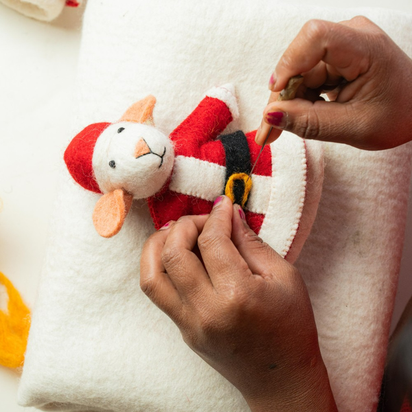 Eine Person filzt eine Weihnachtsdekoration in Form eines Tieres im Weihnachtsmannkostüm.