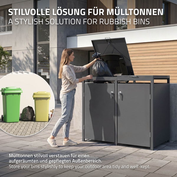 Eine Frau entsorgt einen Müllsack in einer modernen Doppel-Mülltonnenbox aus Metall vor einem Wohnhaus für einen gepflegten Außenbereich.