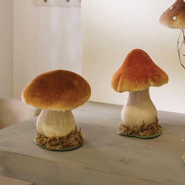 Zwei dekorative Pilzfiguren aus Kunststoff auf einer Holzoberfläche als herbstliche Tischdekoration.