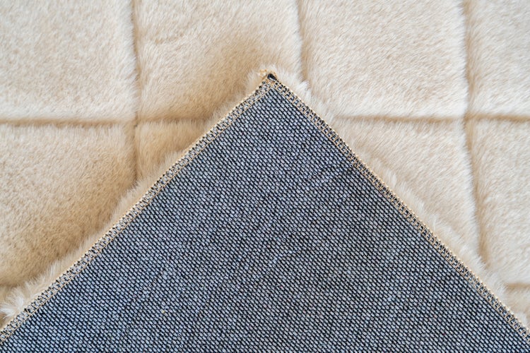 Nahaufnahme eines Teppichs mit weicher Oberfläche in quadratischer Steppoptik und gewebter Rückseite.