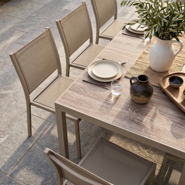 Moderner Gartentisch mit Holzoptik-Platte und Metallgestell sowie Gartenstühle mit Textilbespannung auf einer hellen Terrasse.