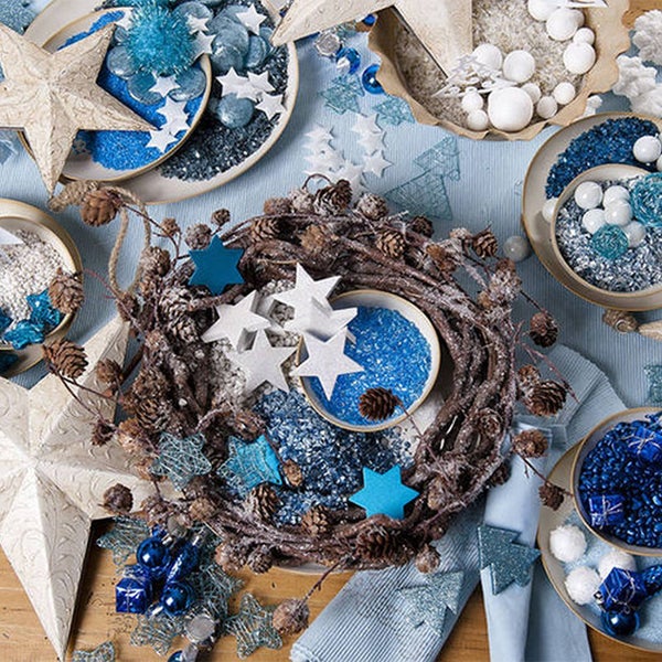 Weihnachtliche Tischdekoration mit einem Kranz aus Zweigen und Zapfen, blauen und weißen Sternen sowie Dekogranulat.