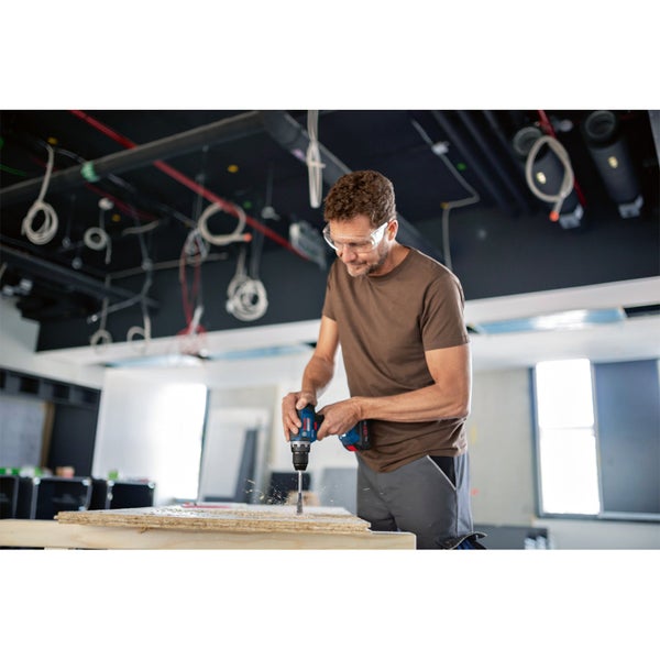 Ein Mann bohrt mit einer Bohrmaschine ein Loch in ein Holzbrett.