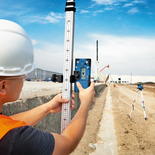 Bauarbeiter mit Nivellierlatte und Digitalnivelliergerät auf einer Baustelle