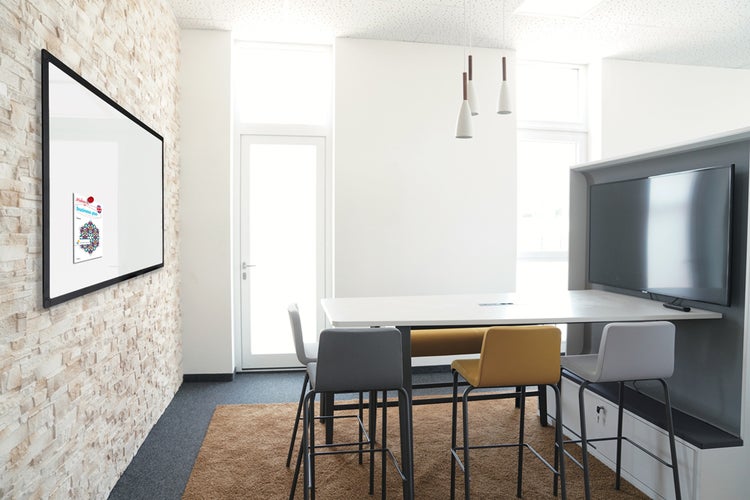 Großes Whiteboard mit schwarzem Rahmen an einer Natursteinwand in einem hellen Besprechungsraum mit hohem Tisch und Barhockern.