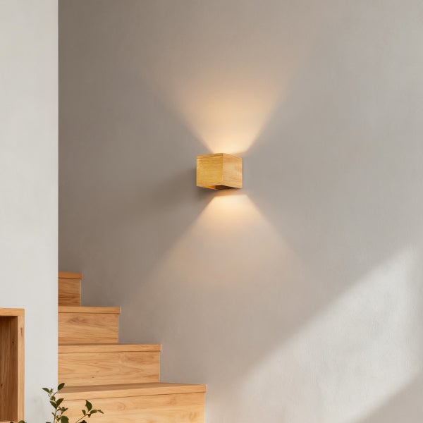 Wandleuchte aus Holz in Würfelform an einer Treppenhauswand mit warmem Up and Down Lichteffekt.