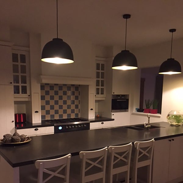 Küchenszene mit drei Hängelampen über einer Kochinsel, weißen Schränken und Schachbrettfliesen