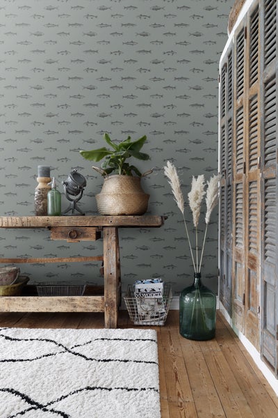 Dekorative Szene mit einem Holztisch, Zimmerpflanze, Glasvase mit Federn und einer Wand mit Fischmuster-Tapete.