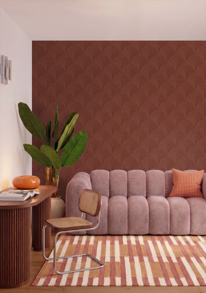 Wohnzimmer mit Tapete in geometrischem Bogenmuster, einem rosa Sofa, einem hölzernen Schreibtisch und einem gemusterten Teppich.
