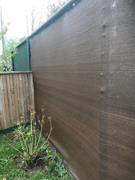 Dunkelbraunes Sichtschutznetz aus Kunststoffgewebe an einem Maschendrahtzaun im Garten montiert.