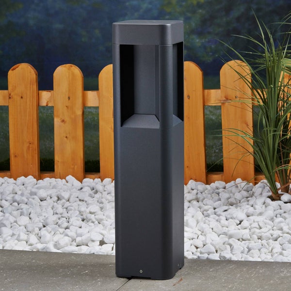 Anthrazitfarbene eckige Wegeleuchte für den Außenbereich, platziert vor einem Holzzaun auf weißem Kies.
