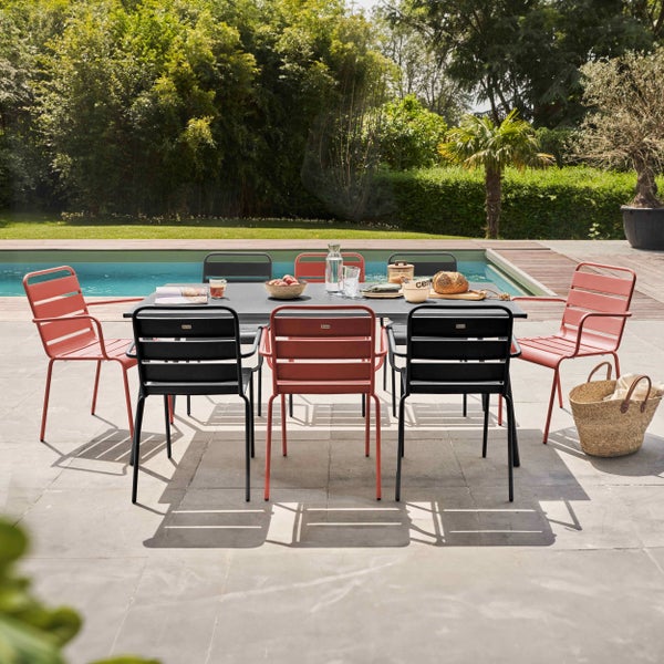 Gartenmöbel-Set mit einem großen Esstisch und Metallstühlen mit Querstreben auf einer hellen Steinterrasse an einem Pool.