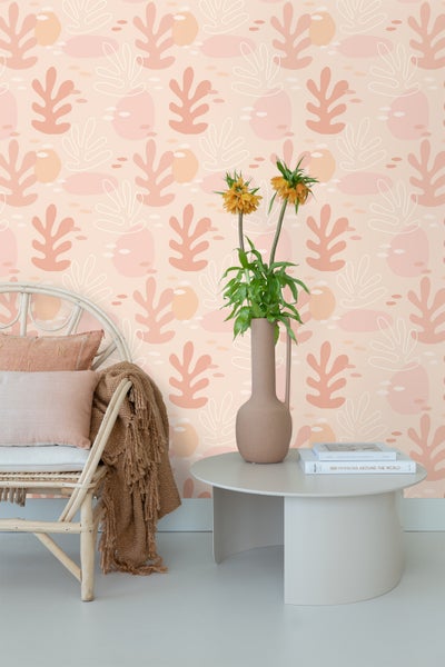 Ein Raum mit einer weißen Rattancouch, einer Vase mit Blumen auf einem runden Tisch und einer Tapete mit Blättermuster