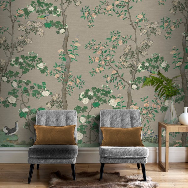 Vlies-Tapete mit floralem Chinoiserie-Muster und Vogelmotiven, präsentiert in einem Wohnraum mit zwei grauen Sesseln und Holztisch.