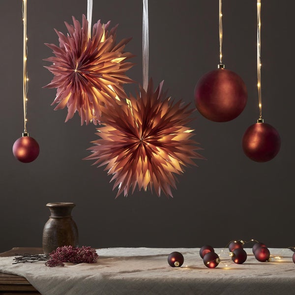 Dekorative Szene mit Papiersternen, Weihnachtskugeln und Lichterketten auf einem Tisch