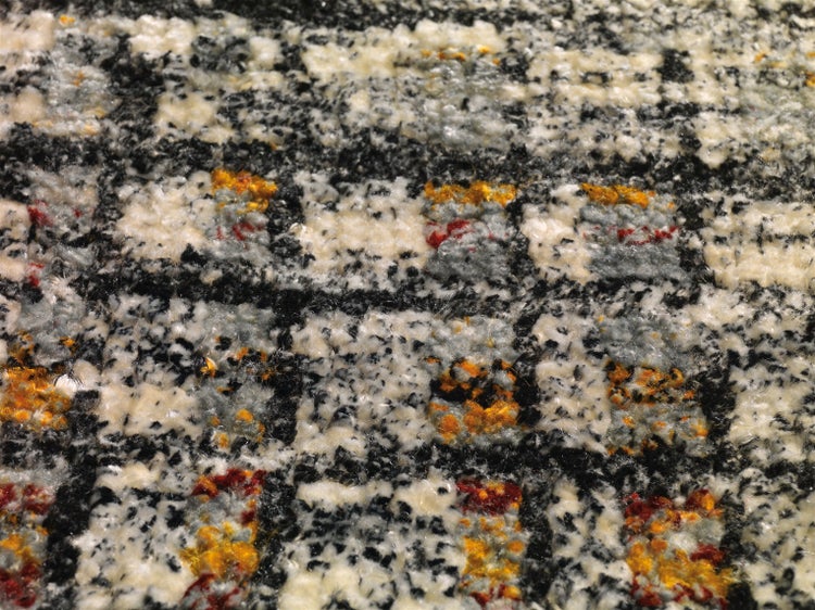 Nahaufnahme eines gemusterten Teppichs mit weicher, strukturierter Oberfläche und Karodesign in Schwarz, Weiß, Grau und Orange.