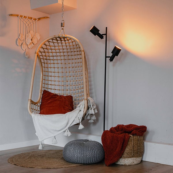 Eckansicht eines Zimmers mit Hängesessel, Stehlampe, Korb, Teppich und Pouf.