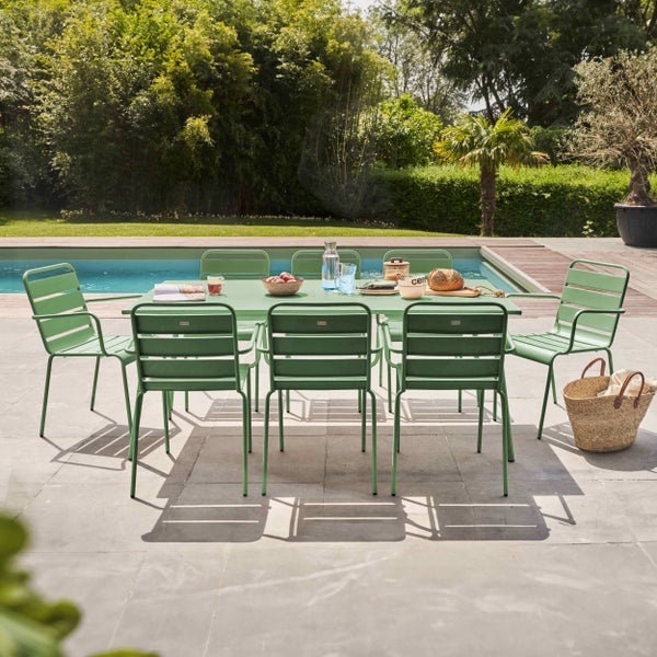 Gartenmöbel Set aus grünem Metall mit rechteckigem Tisch und sechs Stühlen auf einer Steinterrasse am Pool in einem hellen Garten.