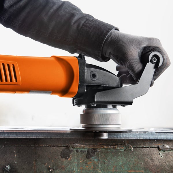 Person bearbeitet eine Metallkante mit einer orangefarbenen Kantenfräse, eine Hand im grauen Schutzhandschuh führt das Gerät.