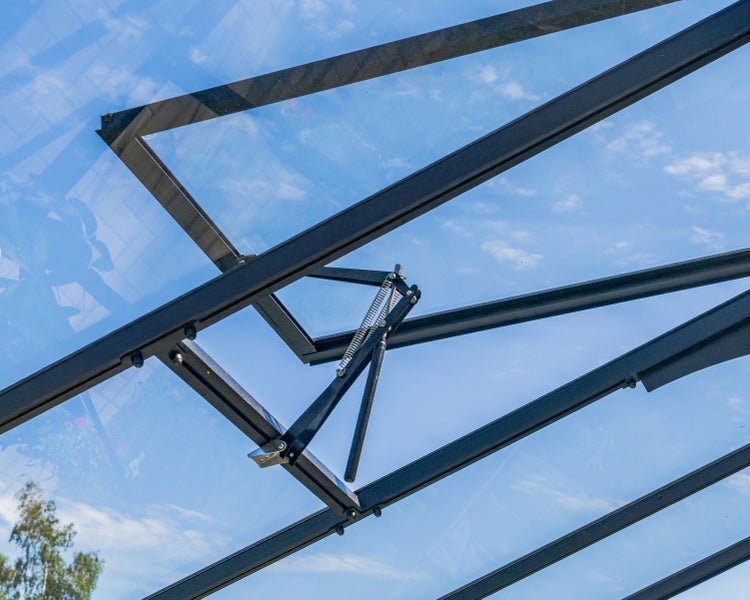 Automatischer Fensteröffner für Gewächshäuser an einem schwarzen Dachfensterrahmen montiert.