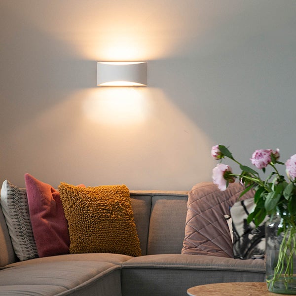 Wohnzimmer mit Sofa, Kissen, Tisch und einer weißen Wandleuchte