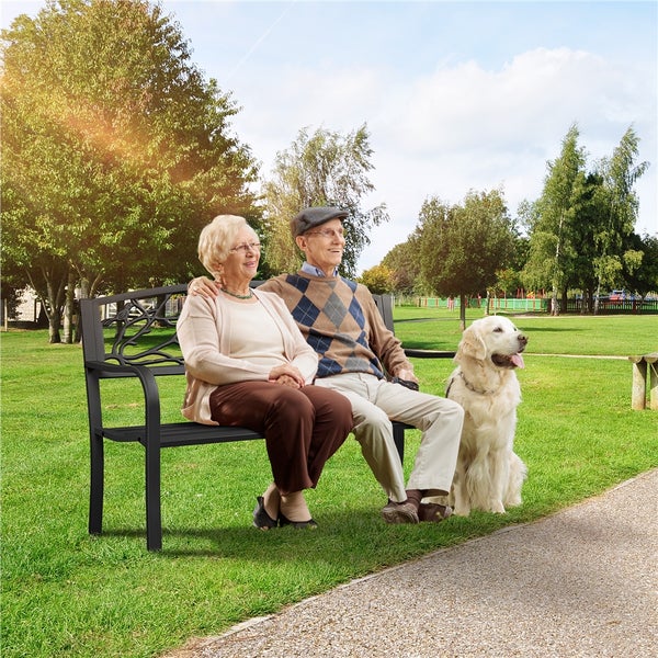 Ein älteres Paar sitzt mit einem Hund auf einer Parkbank.