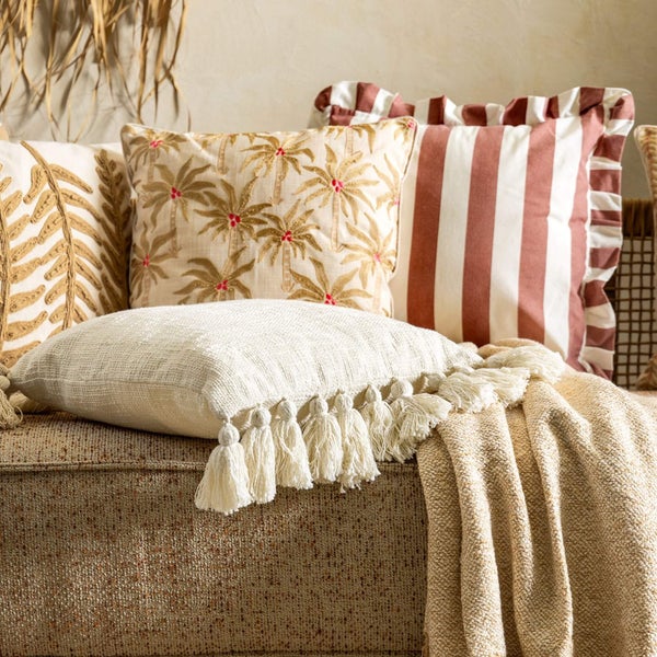 Dekorative Kissen mit unterschiedlichen Mustern liegen auf einem Sofa mit beiger Decke.