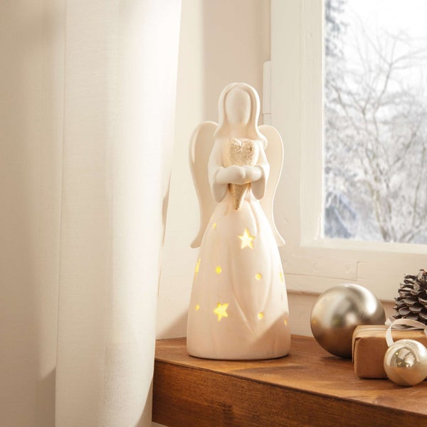 Dekorative Engel-Figur mit Herz und Sternenmuster auf einer Fensterbank mit Weihnachtsdekoration.