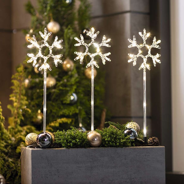 Dekorative Schneeflockenleuchten im Beet mit Weihnachtsbaum im Hintergrund