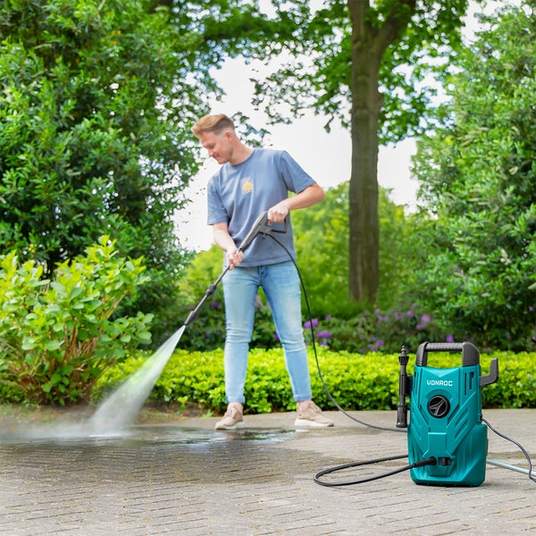 Frau reinigt PKW mit Hochdruckreiniger auf gepflasterter Einfahrt im Außenbereich.