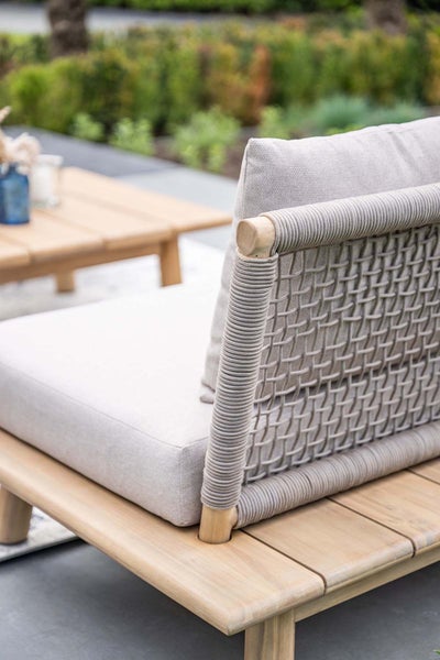 Garten-Loungesessel aus hellem Holz mit Rückenlehne aus Seilgeflecht und hellen Polstern auf einer Terrasse.