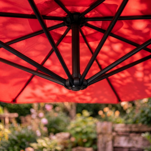 Unteransicht eines roten Sonnenschirms mit schwarzem Metallgestell und Streben in einem Garten.