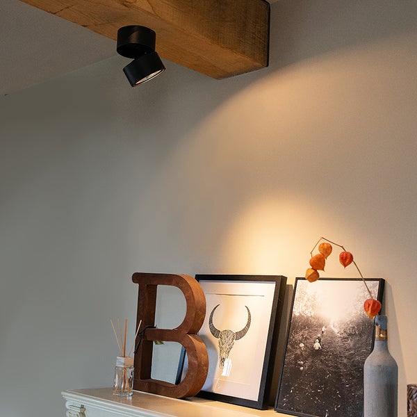 Zwei schwarze Aufbaustrahler an einer Holzbalkendecke über einem dekorierten Regal