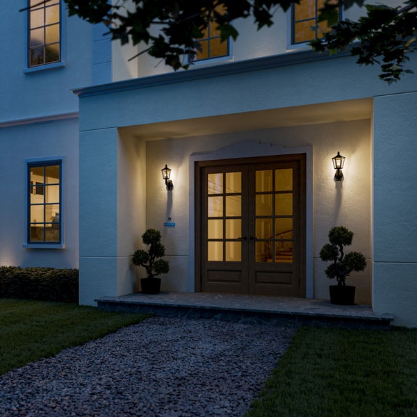 Beleuchtete klassische Außenwandleuchten neben einer hölzernen Doppeltür an einem Hauseingang bei Dämmerung.