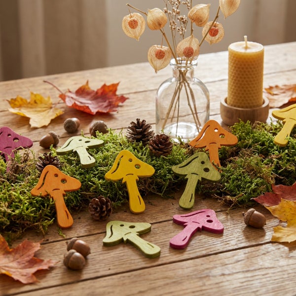 Herbstliche Tischdekoration mit hölzernen Pilzfiguren, Moos, Eicheln, Tannenzapfen, Blättern, Lampionblumen in einer Vase und einer Bienenwachskerze.